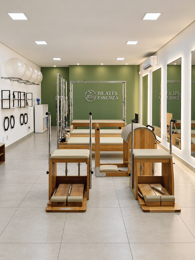 Estúdio Pilates Essenza com Step Chairs, Reformers, Cadillac e espelhos diante da parede verde com o logo